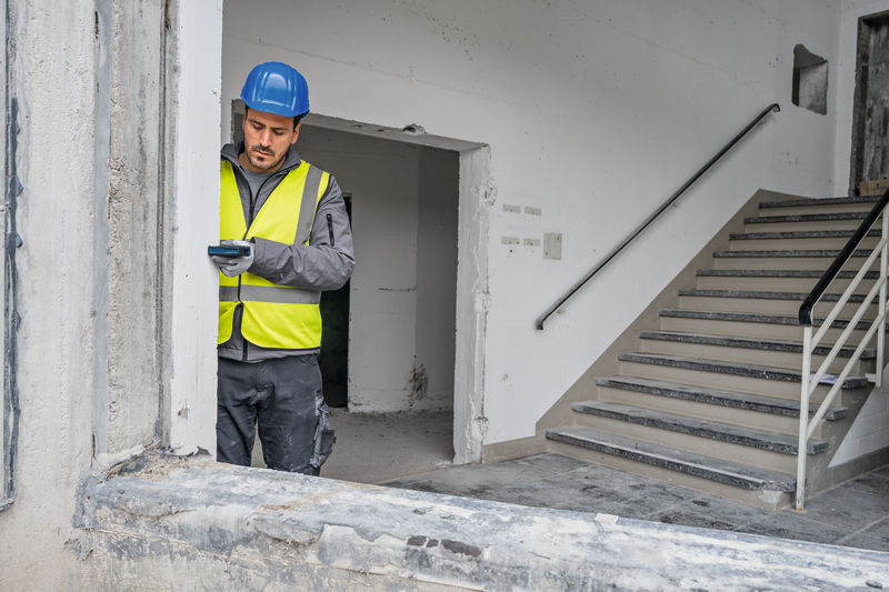 Eine Person mit Sicherheitsausrüstung misst eine Fensteröffnung mit einem Lasermessgerät. Anwendungsbild