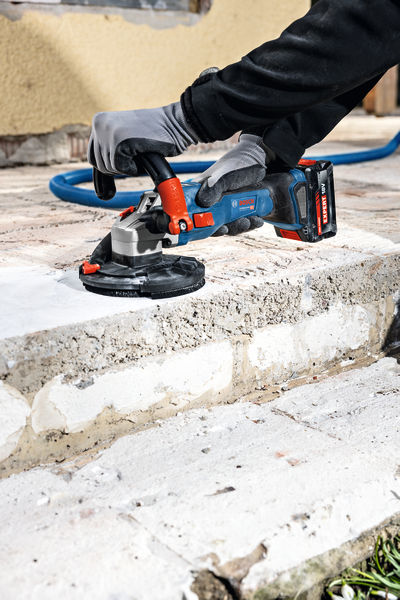 Eine Person mit Schutzausrüstung schleift Betonstufen mit einem Akku-Betonschleifer. Anwendungsbild