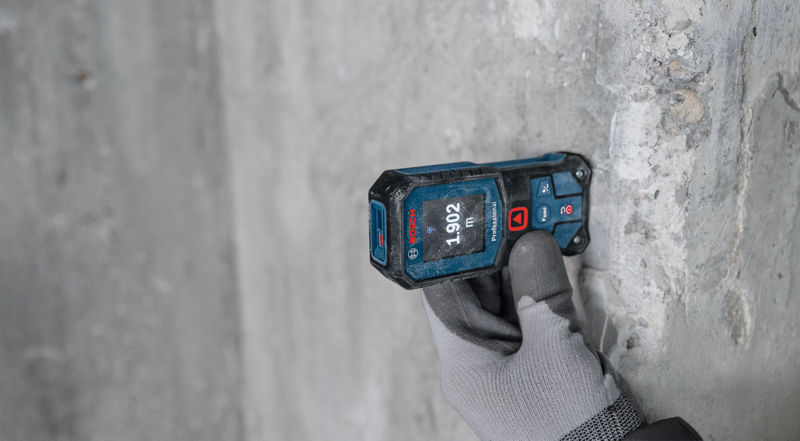 Eine Person mit Handschuhen verwendet ein Lasermessgerät an einer Betonwand. Anwendungsbild