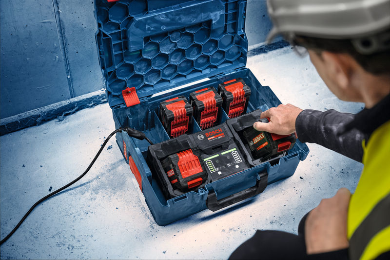 Eine Person mit Sicherheitsausrüstung bedient auf einer Baustelle eine Ladestation für mehrere Batterien. Anwendungsbild