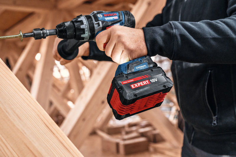 Eine Person, die mit einer Akkubohrmaschine eine Schraube in Holz dreht. Anwendungsbild