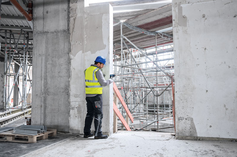 Eine Person mit Sicherheitsausrüstung verwendet ein Lasermessgerät, um Abstände auf einer Baustelle zu überprüfen. Anwendungsbild
