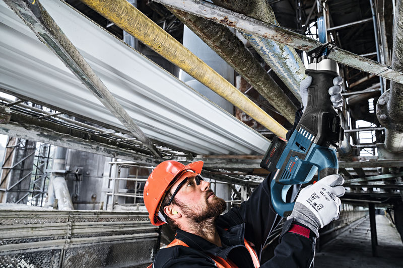 Eine Person mit Sicherheitsausrüstung schneidet über dem Kopf mit einer Säbelsäge ein Metallrohr durch. Anwendungsbild