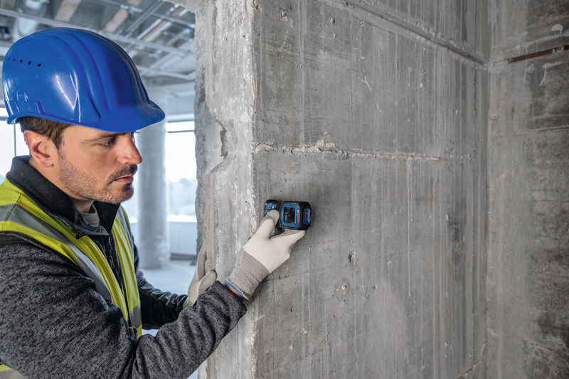 Eine Person mit Sicherheitsausrüstung verwendet ein Lasermessgerät an einer Betonwand. Anwendungsbild