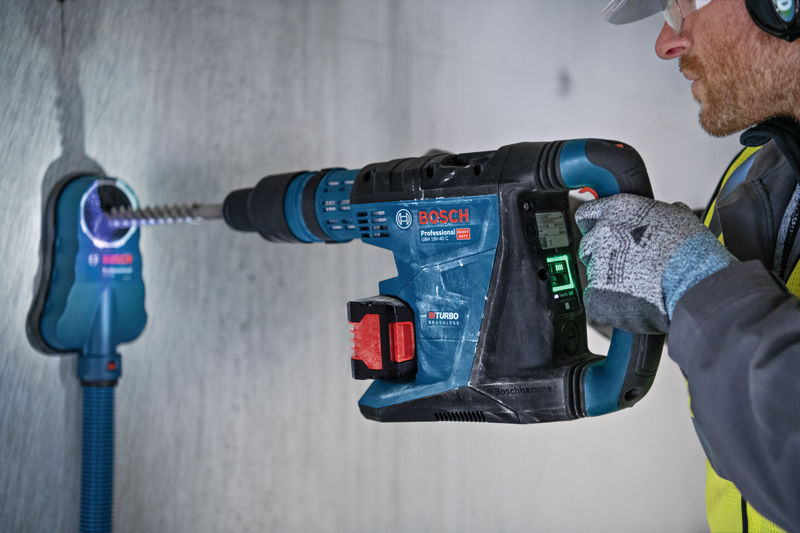 Eine Person mit Sicherheitsausrüstung bohrt mit einem Elektrowerkzeug und einem Staubabsauger in Beton. Anwendungsbild