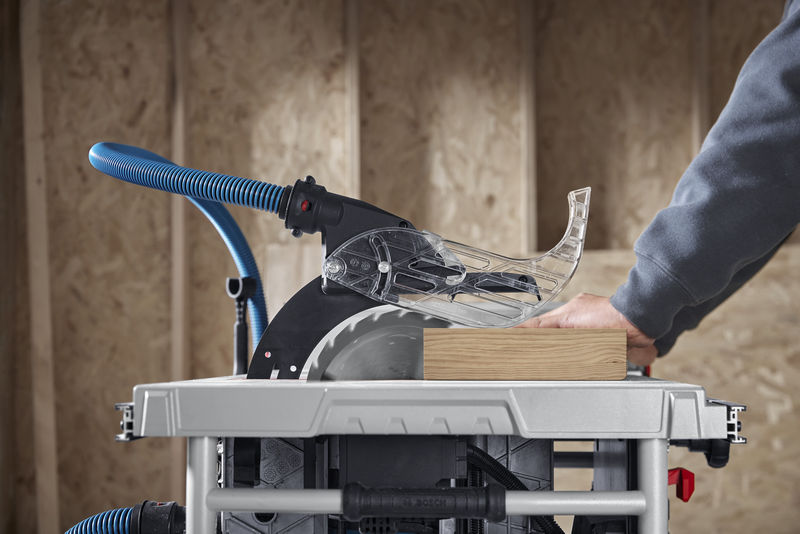 Eine Person führt in einer Werkstatt Holz durch eine Tischkreissäge mit Staubabsaugung. Anwendungsbild Nahaufnahme