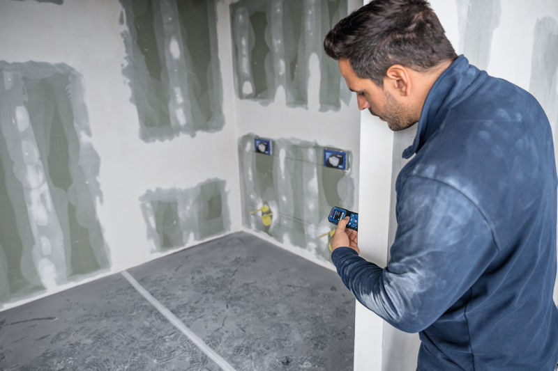 Eine Person verwendet ein Lasermessgerät, um die Entfernung in einem im Bau befindlichen Raum zu überprüfen. Anwendungsbild