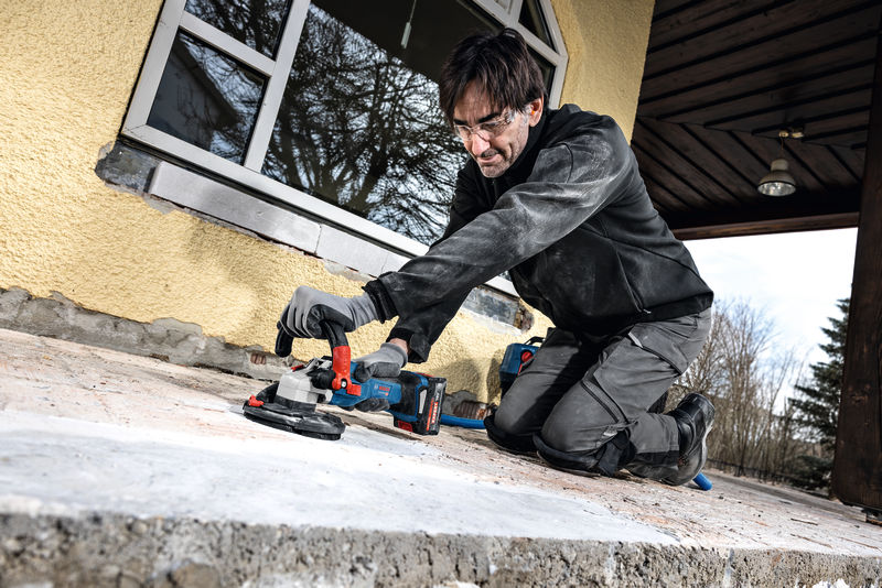 Eine Person mit Sicherheitsausrüstung schleift eine Betonoberfläche mit einem Elektrowerkzeug. Anwendungsbild