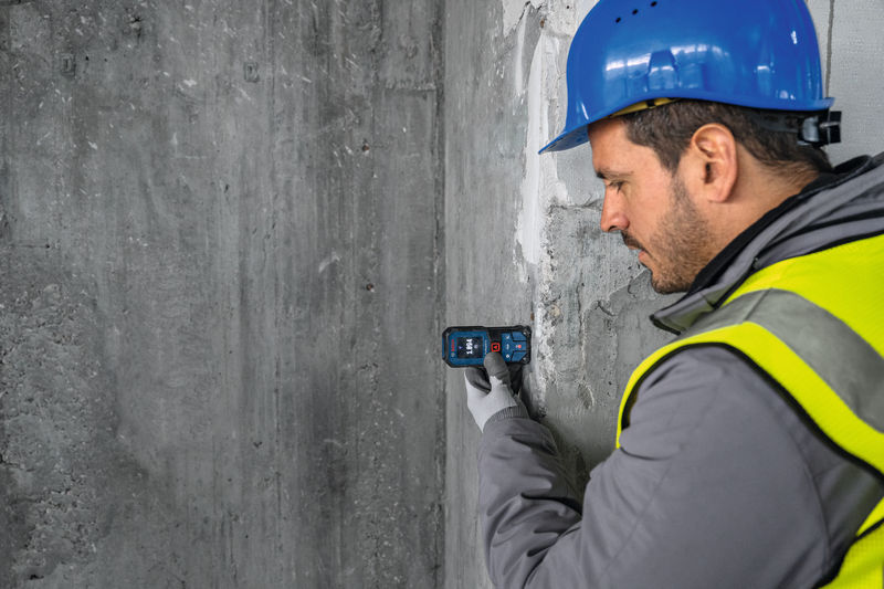 Eine Person mit Sicherheitsausrüstung verwendet ein Lasermessgerät an einer Betonwand. Anwendungsbild