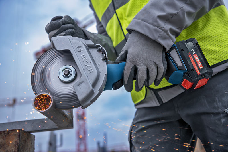 Eine Person mit Sicherheitsausrüstung schneidet Metallrohre mit einem Akku-Winkelschleifer. Anwendungsbild