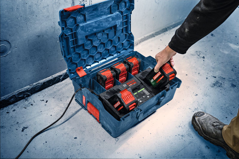 Eine Person legt eine Batterie in eine tragbare Ladestation auf dem Boden einer Werkstatt. Anwendungsbild