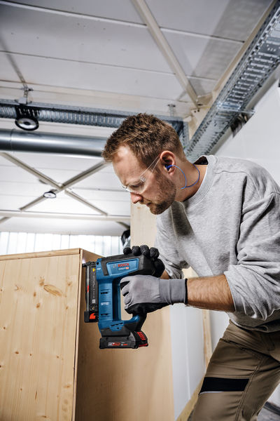 Eine Person mit Sicherheitsausrüstung verwendet eine Stichsäge, um in einer Werkstatt Holz zu schneiden. Anwendungsbild