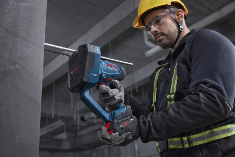 Eine Person mit Schutzausrüstung schneidet eine Gewindestange mit einem Akku-Stangenschneider. Anwendungsbild